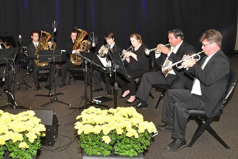 Brass ensemble performing on a stage lined with yellow flowers