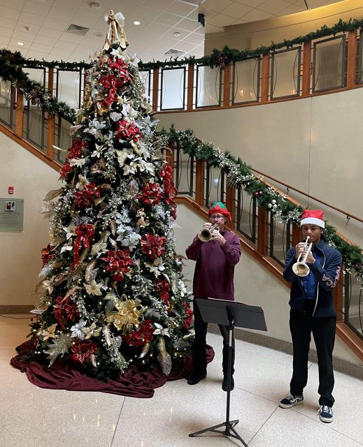 Holiday trumpet duets beside a Christmas tree