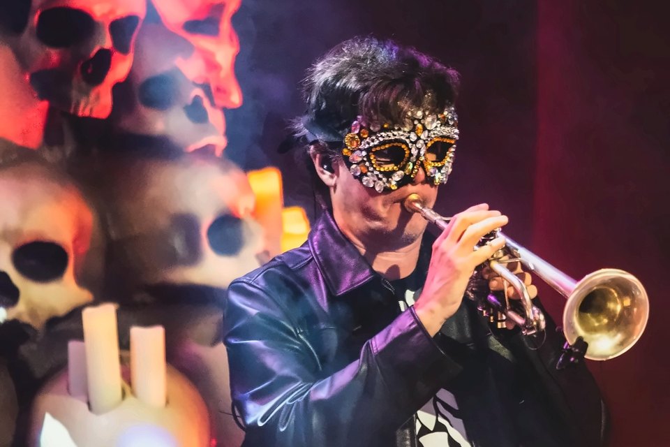 Luis Engelke in a jeweled mask playing trumpet in a spotlight