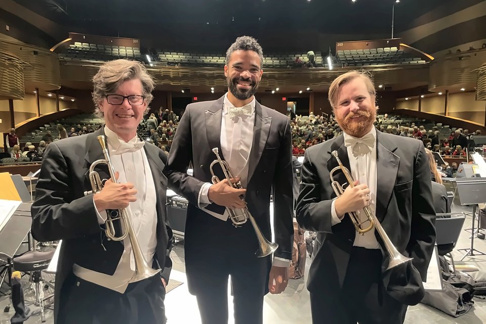Luis Engelke and two trumpeters in white tie holding their trumpets on stage before an audience