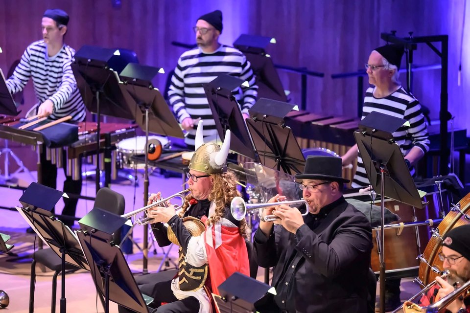 Two trumpeters in costume, one in a Viking helmet, playing with the orchestra